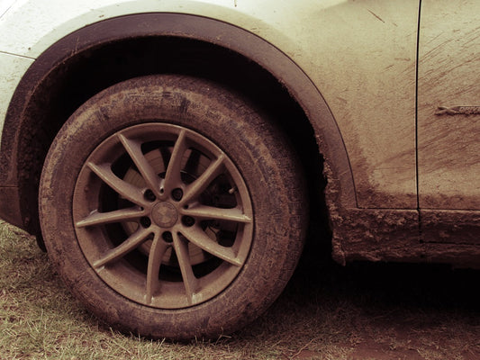 A close-up of a car's muddy wheel and fender, covered in dirt after off-road driving