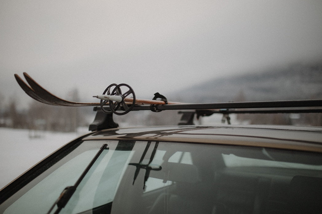 A pair of skis secured to the roof rack of a car with snowy mountains in the background